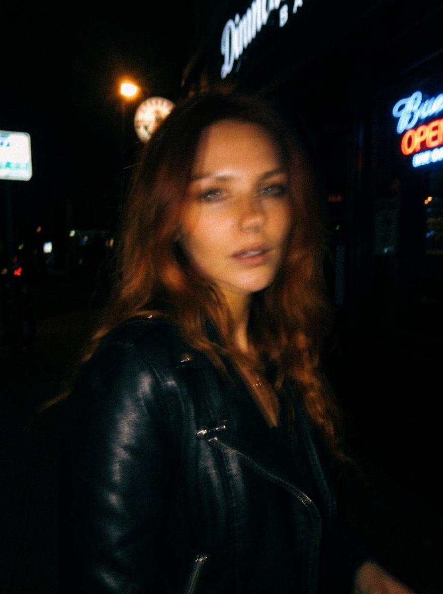 Dark, blurry night photo of a woman in a leather jacket outside a bar