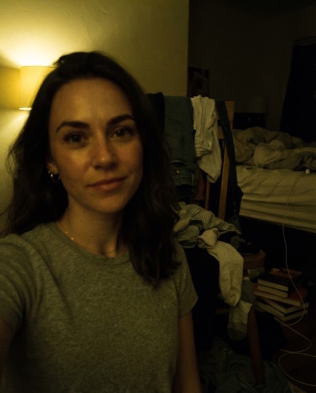 A dark, yellow, grainy selfie in a messy room, used as the starting photo for the fix prompts